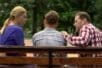 Two parents sit on a bench with their teen